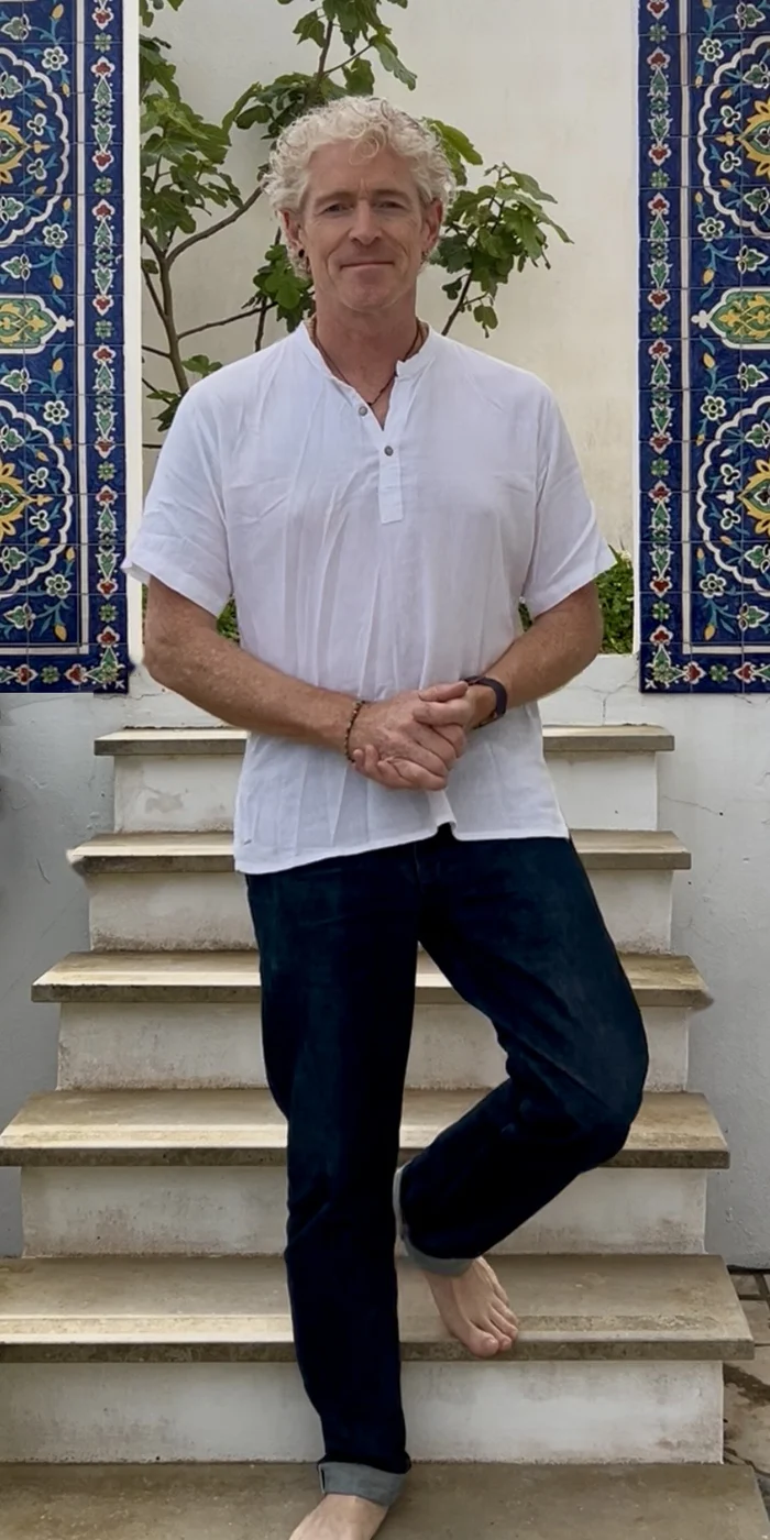 Phil in a white shirt standing on stone steps between blue tiled panels, smiling