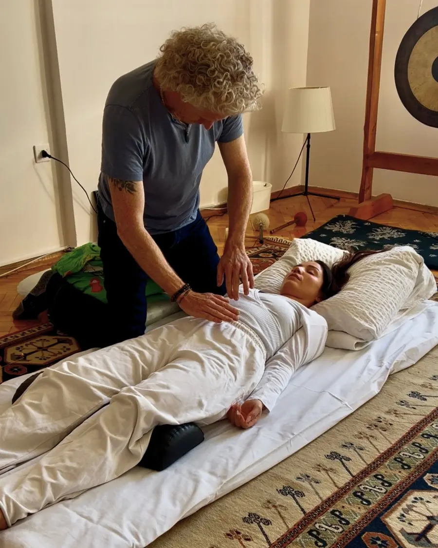 Phil resting his hands on the abdomen of a fully clothed client lying on a mat