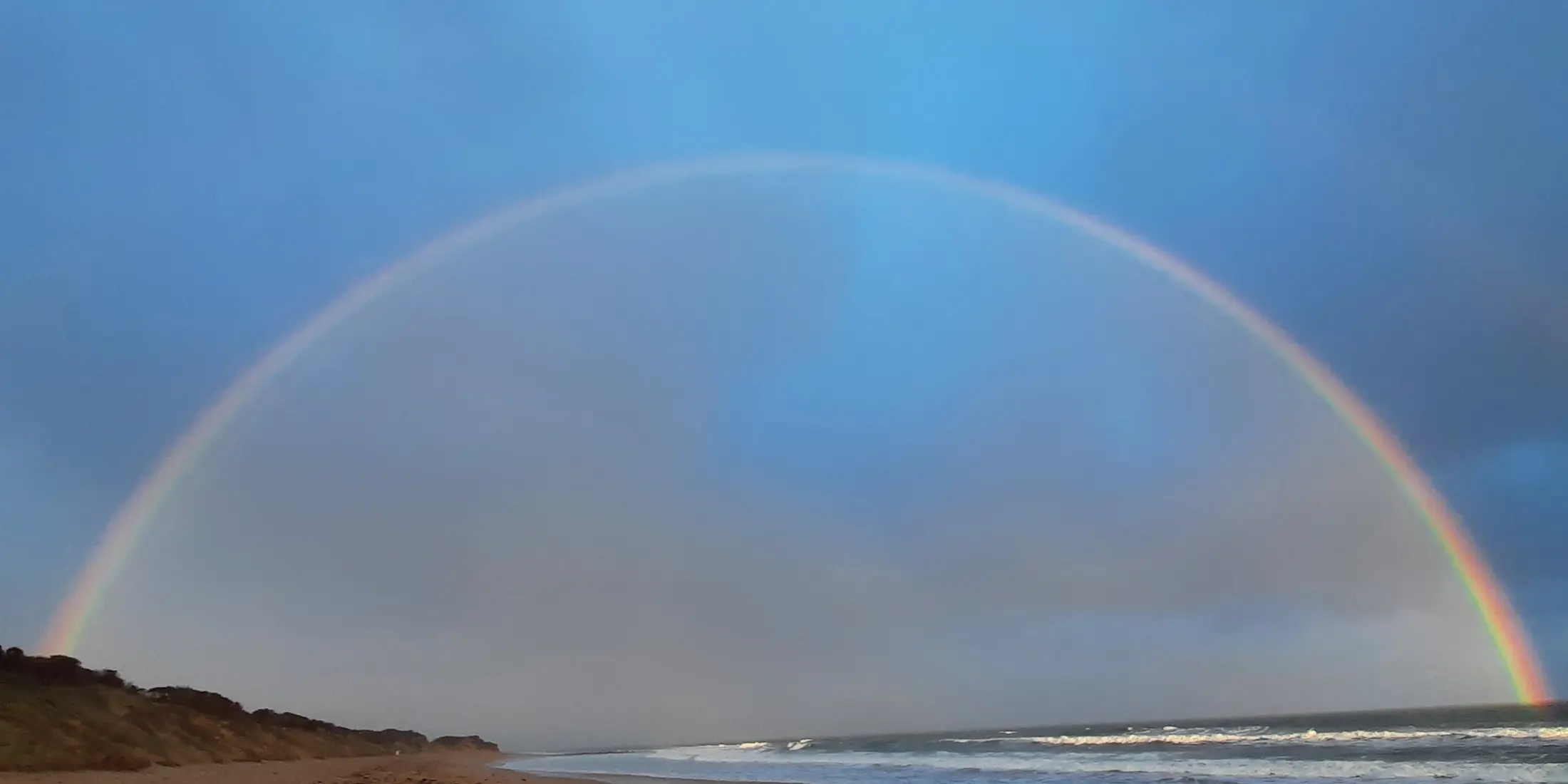 A full rainbow arching over a Surf Coast beach