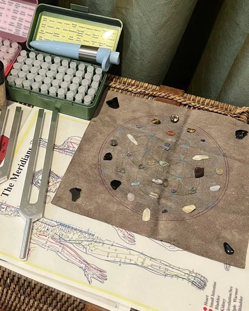 Tuning forks and a crystal grid on a meridian chart, with remedy vials behind