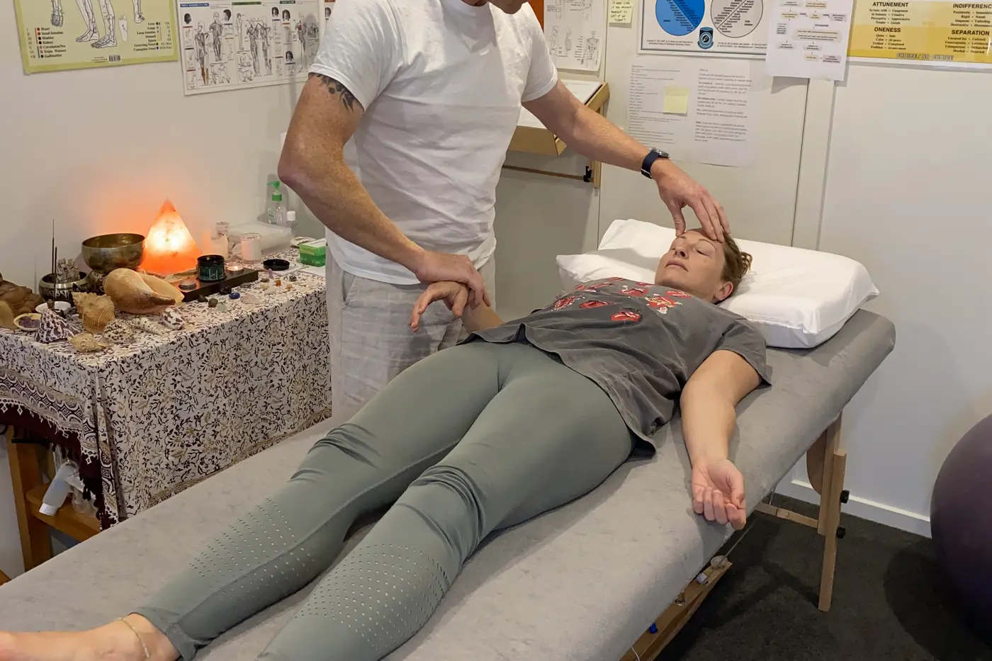 A client lying on a treatment table in a bright white clinic room while Phil works